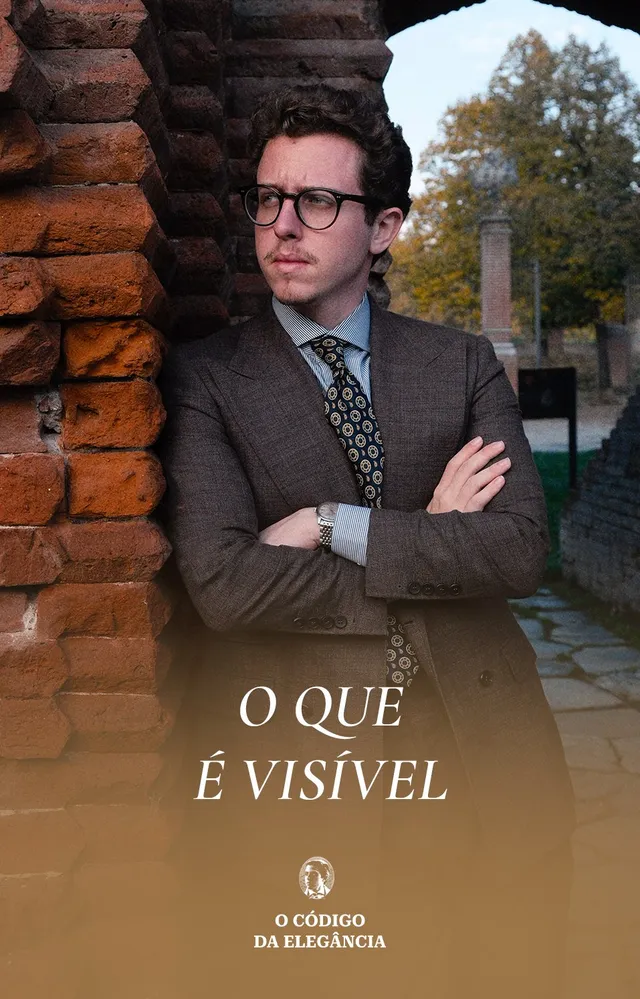 Renzo Schmitz de terno marrom encostado numa parede de tijolos